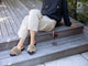 Woman wearing Baza Shearling slide sandal in bronze/black with beige pants and sweater, next to wine glass