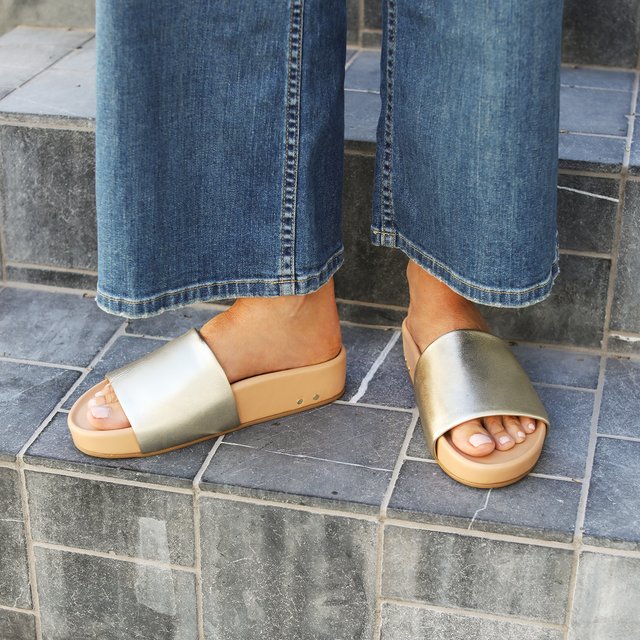 woman wearing Pelican leather slide sandals in platinum/beach with jeans on steps