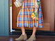 Woman wearing Falcon suede booties in chestnut with plaid dress and jean jacket, holding package and flowers.