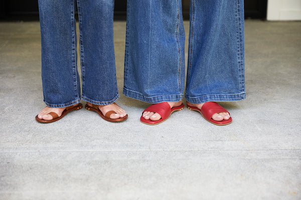 Women wearing Finch leather toe ring sandals in tan and Honeybird leather slide sandals in red with jeans