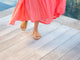 Woman wearing Gallito leather slide sandals in honey with coral dress.