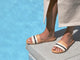 Woman wearing Gallito Stripe leather slide sandal in eggshell/beach with beige dress by the pool