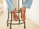 Woman wearing Heron leather ankle strap block heel sandal in tan with jeans on a stool