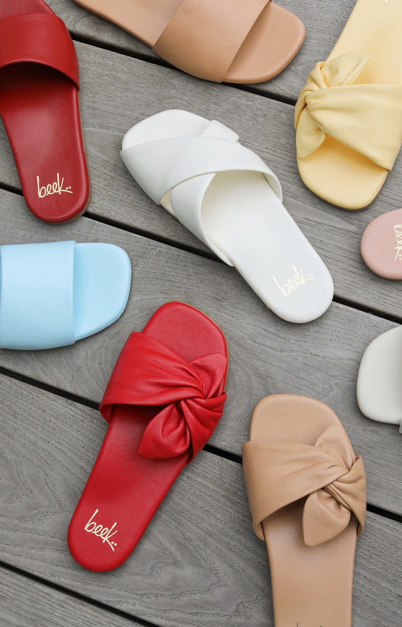 Group shot of Honeybird leather slide sandals in sky, red, beach with Fernbird leather slide sandals in vanilla and Sweetbird leather slide sandals in lipstick and glow.