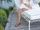 Woman wearing Linnet leather toe-ring sandal in tan with white linen dress on lounge chair