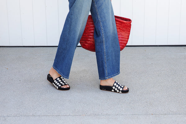 Woman wearing Pelican Woven leather platform sandals in eggshell/black with jeans carrying red woven bag