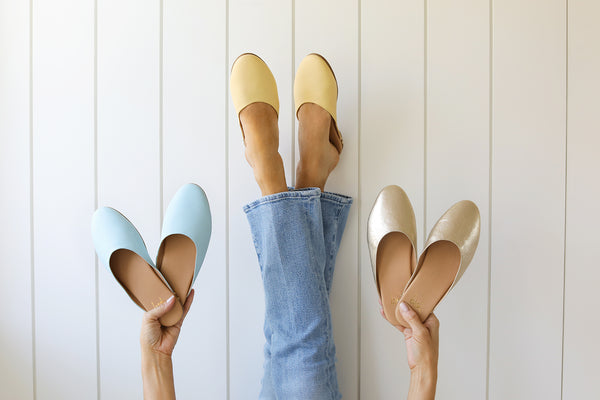 Woman wearing Phoebe leather ballet mule in glow with jeans, holding Phoebe mules in sky and gold