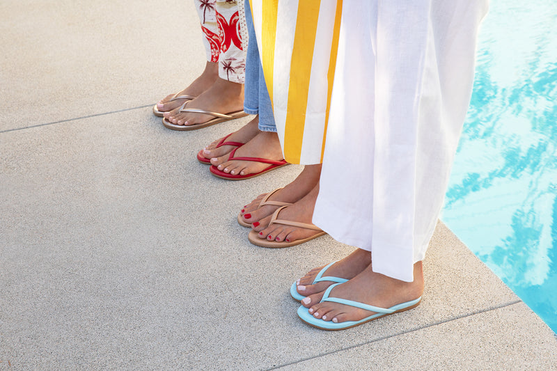 Women wearing Sunbeam leather flip flop sandal in sky, beach, lipstick, and bronze