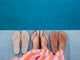 Woman wearing Sunbeam leather flip flop sandal in tan with striped dress next to Sunbeam flip flop sandals in beach and rose gold.