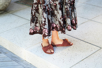 Woman wearing Tesia suede slide sandal in fig with skirt